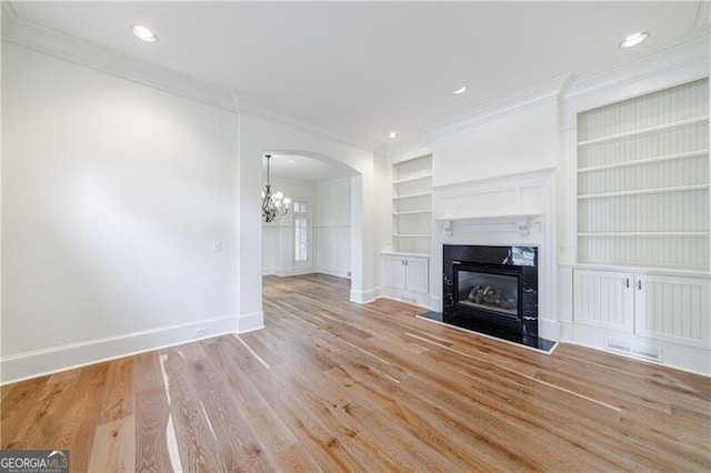 unfurnished living room with a high end fireplace, built in shelves, crown molding, light hardwood / wood-style flooring, and a chandelier