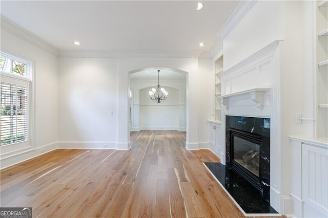 unfurnished living room with crown molding, light hardwood / wood-style flooring, a high end fireplace, and a chandelier