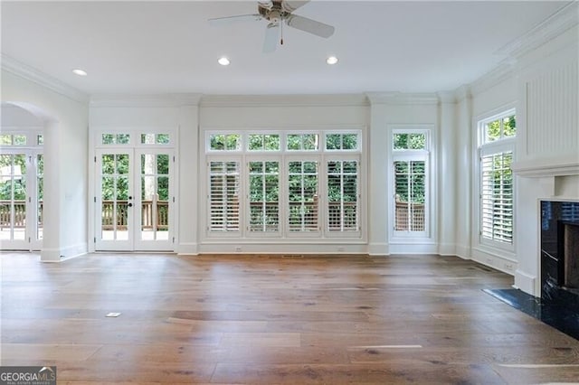 unfurnished living room featuring ceiling fan, french doors, crown molding, a fireplace, and hardwood / wood-style flooring