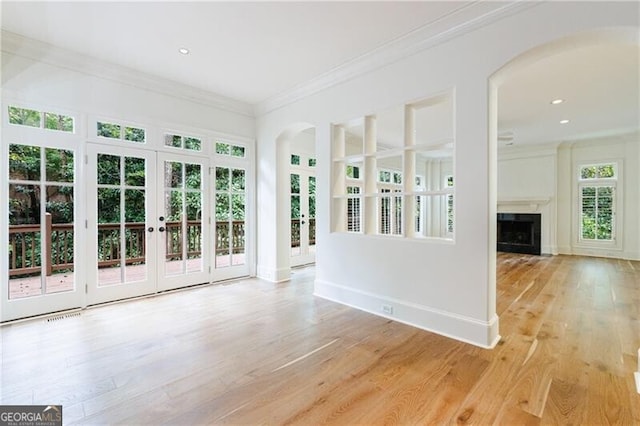 unfurnished living room with a healthy amount of sunlight, light wood-type flooring, and crown molding