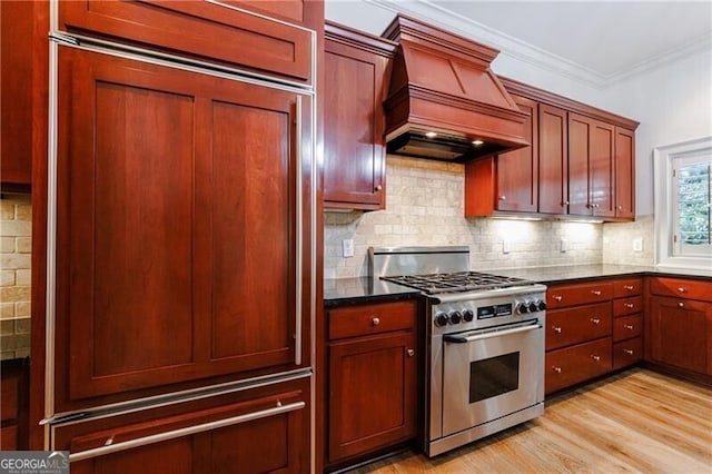 kitchen featuring tasteful backsplash, custom range hood, high end stainless steel range oven, crown molding, and light hardwood / wood-style floors