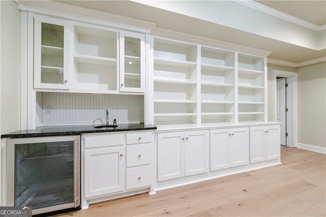 bar with sink, light wood-type flooring, ornamental molding, white cabinetry, and beverage cooler