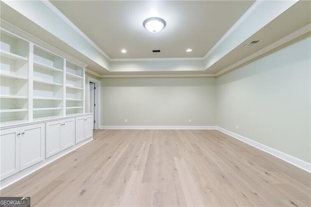 empty room featuring light wood-type flooring, ornamental molding, and a tray ceiling