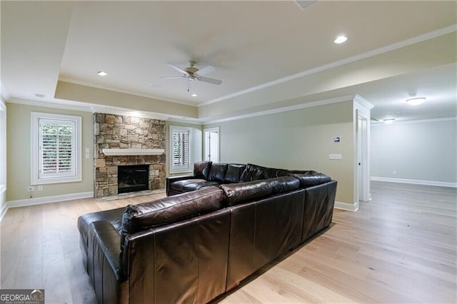 living room featuring a stone fireplace, ceiling fan, ornamental molding, and light wood-type flooring