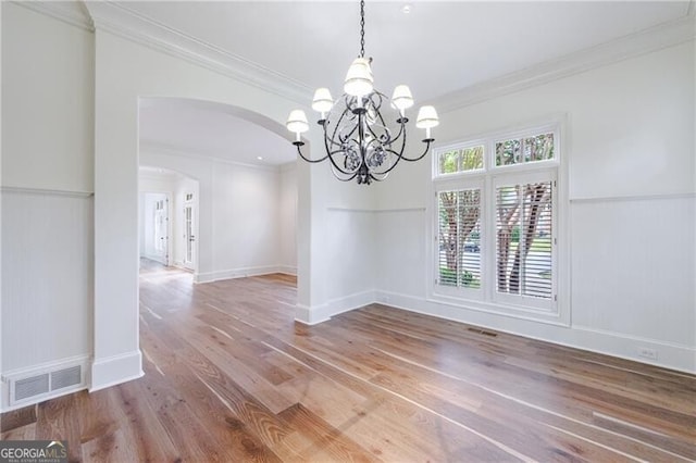 unfurnished dining area featuring wood-type flooring, ornamental molding, and an inviting chandelier