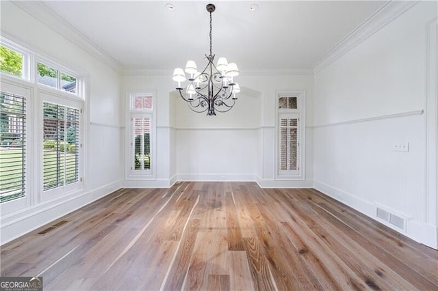 unfurnished dining area with crown molding, hardwood / wood-style floors, a healthy amount of sunlight, and a notable chandelier