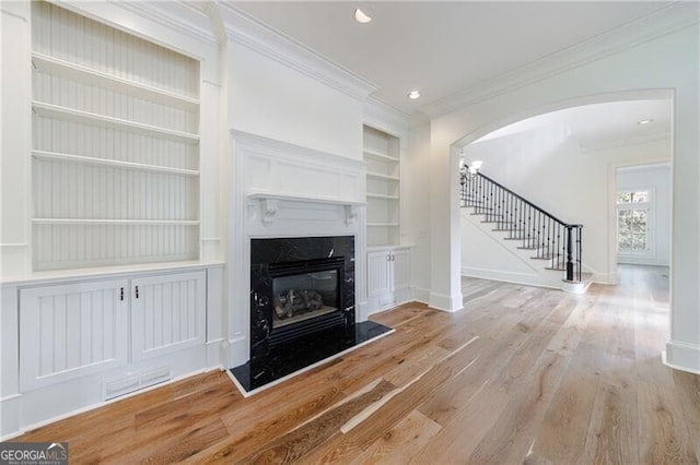 unfurnished living room featuring light hardwood / wood-style floors, a premium fireplace, ornamental molding, and built in features