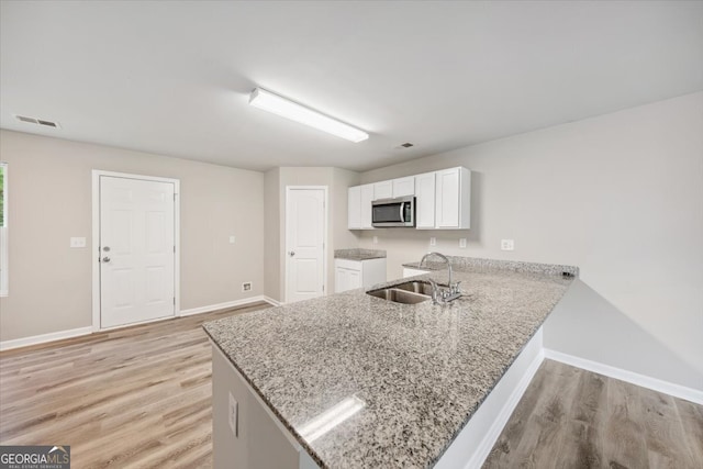 kitchen featuring light stone counters, sink, white cabinets, kitchen peninsula, and light hardwood / wood-style flooring