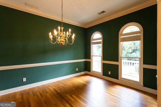 empty room with wood-type flooring, crown molding, and an inviting chandelier