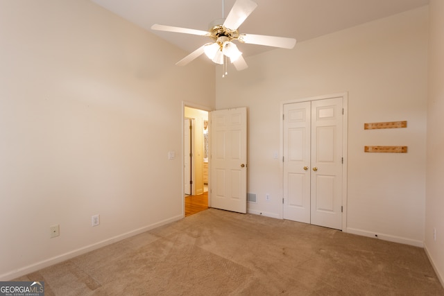 unfurnished bedroom with ceiling fan, a closet, carpet flooring, and high vaulted ceiling