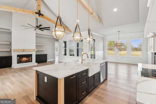 kitchen featuring decorative light fixtures, sink, a large fireplace, light stone counters, and a center island with sink