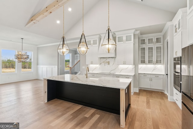 kitchen featuring white cabinetry, light wood-type flooring, pendant lighting, light stone countertops, and a kitchen island with sink