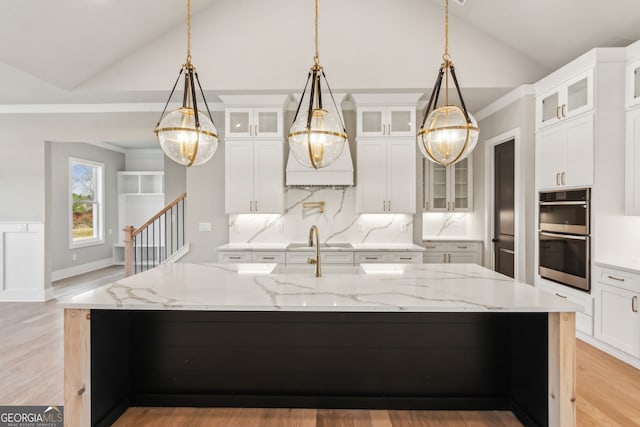 kitchen with stainless steel double oven, decorative light fixtures, light stone countertops, and a large island with sink