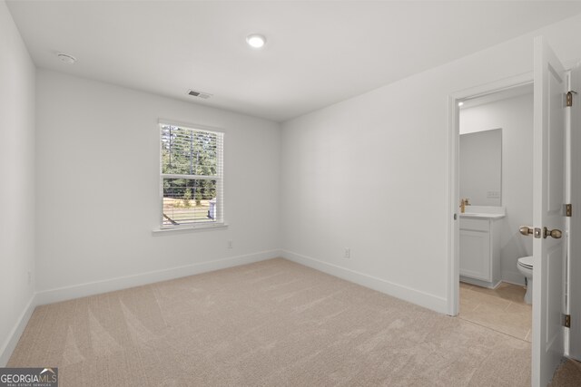 unfurnished bedroom featuring light carpet, connected bathroom, and sink