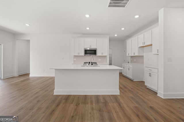 kitchen with a kitchen island with sink, backsplash, white cabinetry, and hardwood / wood-style floors