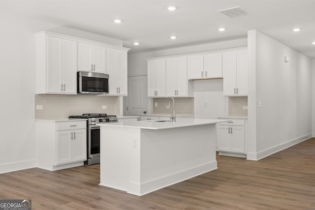 kitchen featuring white cabinetry, hardwood / wood-style floors, appliances with stainless steel finishes, and a kitchen island with sink