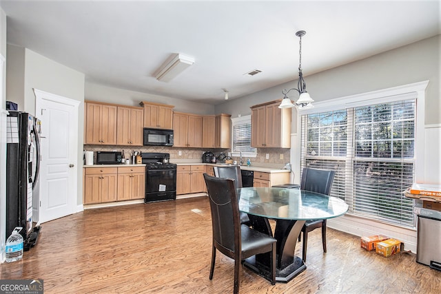 kitchen featuring pendant lighting, light brown cabinetry, light hardwood / wood-style flooring, decorative backsplash, and black appliances