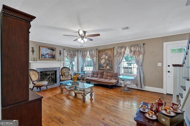 living room featuring a brick fireplace, light hardwood / wood-style floors, ornamental molding, and ceiling fan