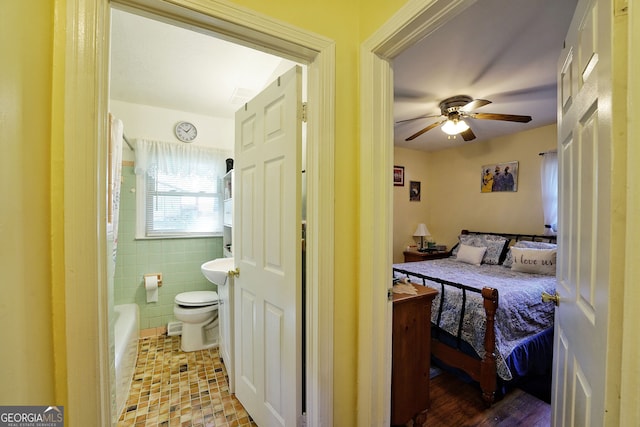 bedroom featuring ceiling fan, light wood-type flooring, tile walls, and ensuite bath