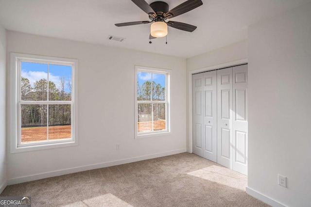 unfurnished bedroom with ceiling fan, light colored carpet, a closet, and multiple windows