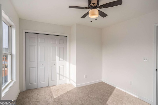 unfurnished bedroom with ceiling fan, a closet, carpet, and multiple windows