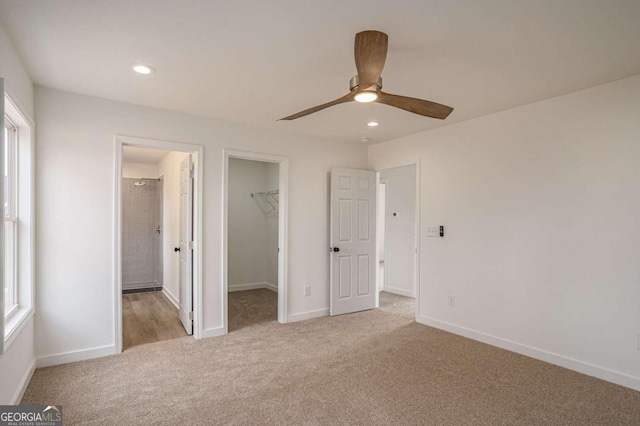 unfurnished bedroom featuring a spacious closet, ceiling fan, light colored carpet, and a closet