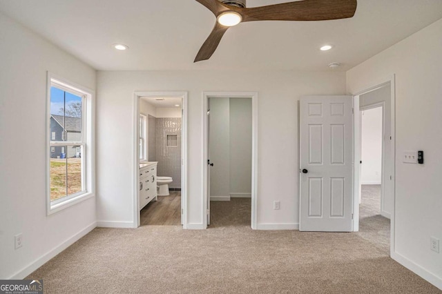 unfurnished bedroom featuring multiple windows, light carpet, ensuite bath, and ceiling fan