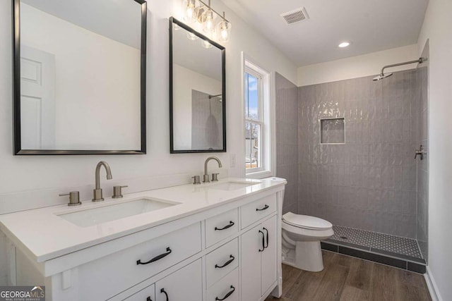 bathroom featuring vanity, hardwood / wood-style flooring, toilet, and tiled shower