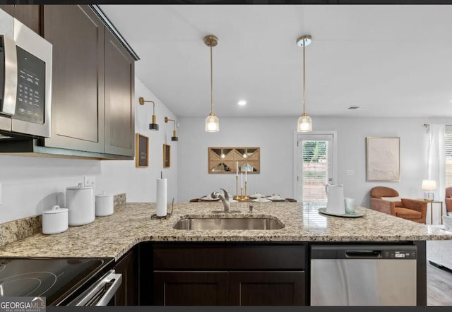 kitchen featuring appliances with stainless steel finishes, open floor plan, a peninsula, dark brown cabinets, and a sink