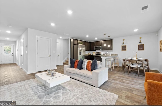 living room with light wood-style flooring, visible vents, stairway, and recessed lighting