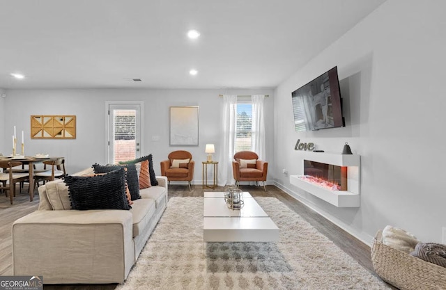 living area with a glass covered fireplace, a healthy amount of sunlight, visible vents, and recessed lighting