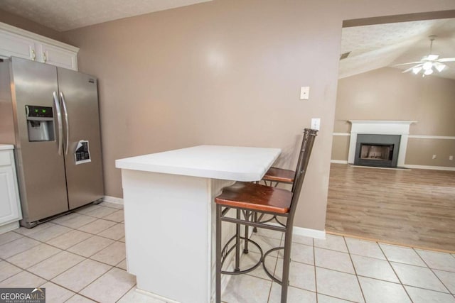 kitchen featuring a kitchen breakfast bar, stainless steel refrigerator with ice dispenser, vaulted ceiling, and white cabinets