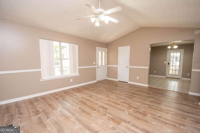 spare room featuring light wood-type flooring, a healthy amount of sunlight, lofted ceiling, and ceiling fan with notable chandelier