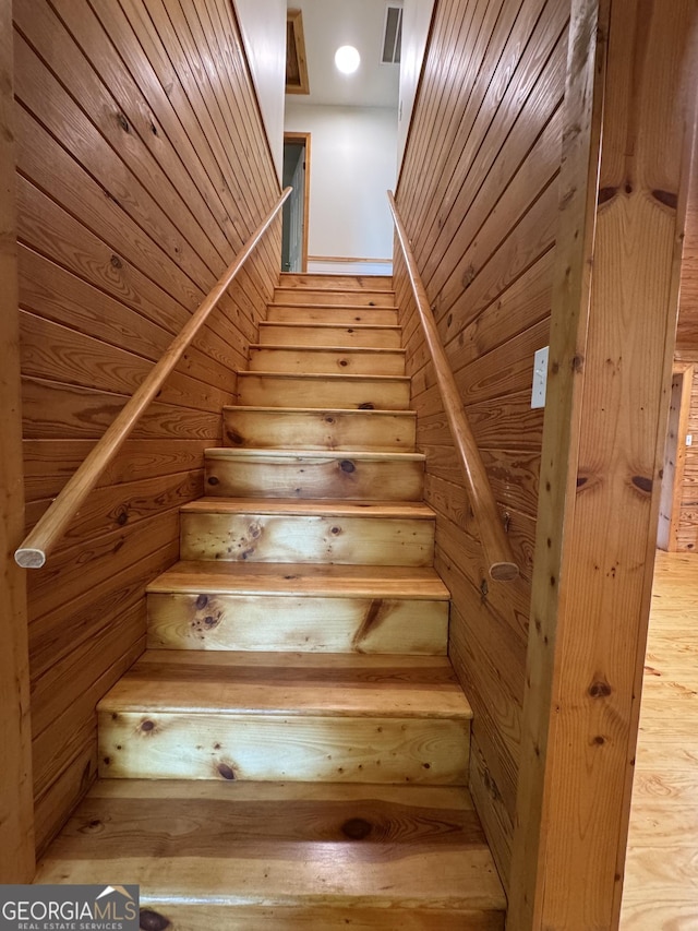 stairway featuring wooden walls and visible vents