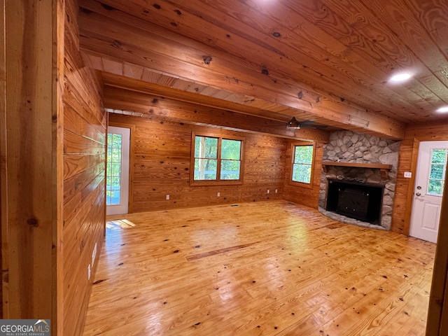 unfurnished living room with light hardwood / wood-style flooring, wooden walls, wooden ceiling, and a stone fireplace