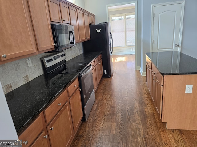 kitchen with dark stone countertops, backsplash, appliances with stainless steel finishes, and dark wood-type flooring