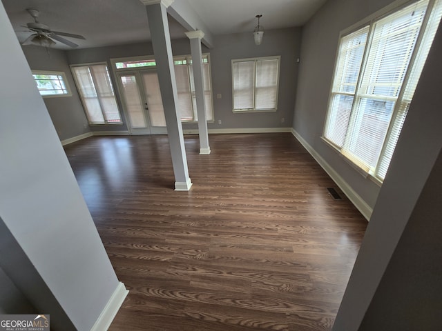 unfurnished living room featuring ceiling fan, dark wood-type flooring, plenty of natural light, and decorative columns