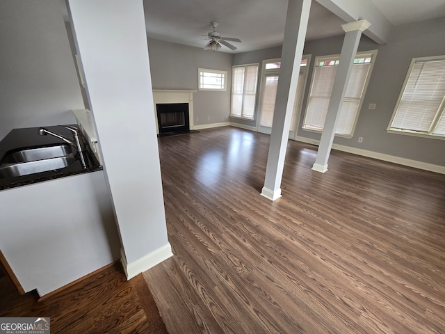 unfurnished living room with ceiling fan, decorative columns, dark hardwood / wood-style floors, and sink