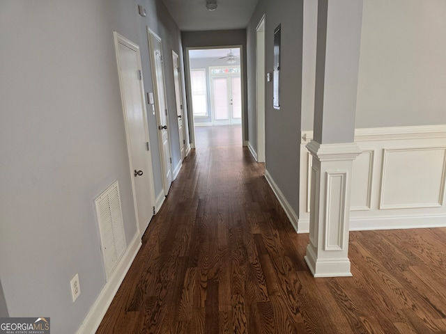 hall featuring ornate columns and dark wood-type flooring