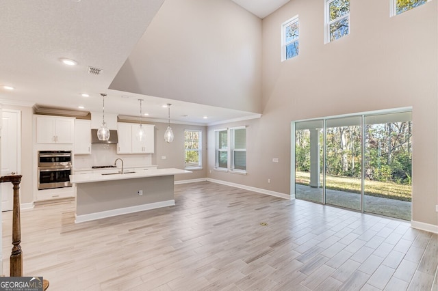 kitchen featuring light wood-type flooring, a center island with sink, decorative light fixtures, white cabinets, and double oven