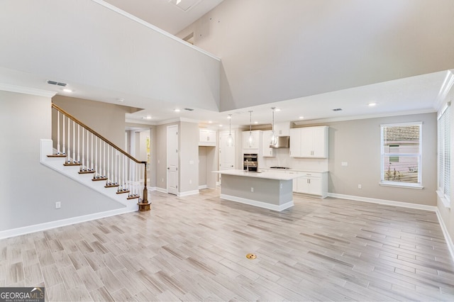 unfurnished living room featuring light wood-type flooring, a high ceiling, and ornamental molding