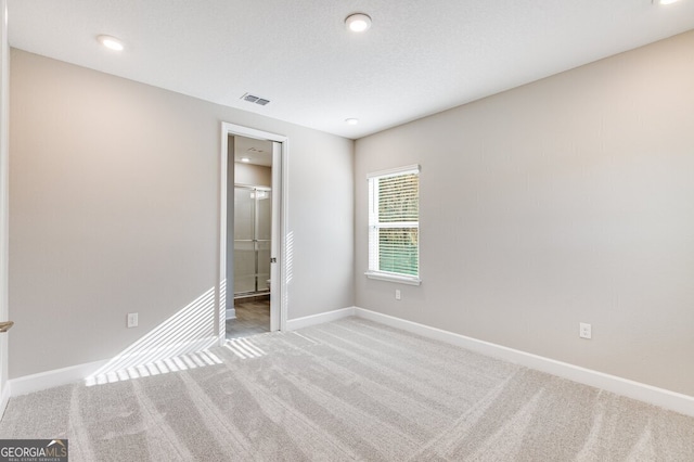 unfurnished bedroom with connected bathroom, light carpet, and a textured ceiling