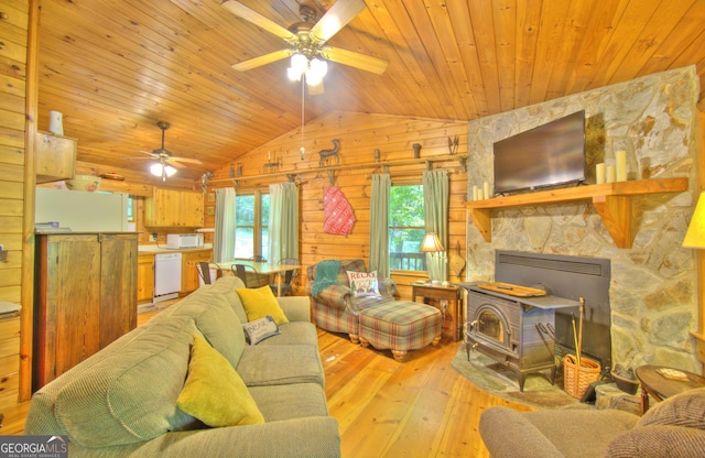 living room with ceiling fan, light wood-type flooring, a wood stove, and vaulted ceiling