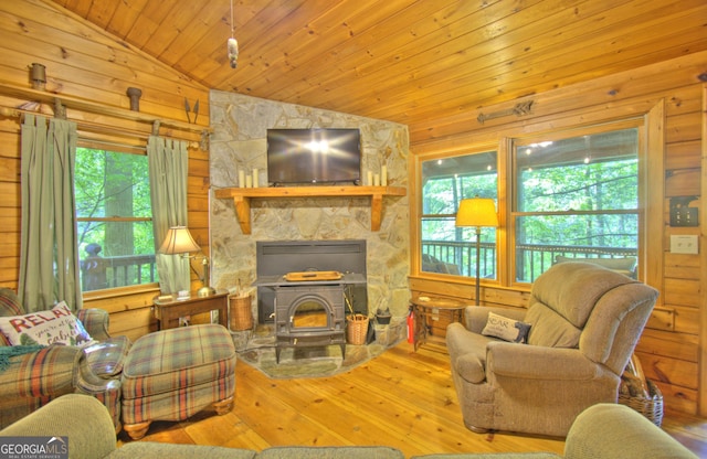 living room with vaulted ceiling, wooden walls, light hardwood / wood-style flooring, wooden ceiling, and a wood stove