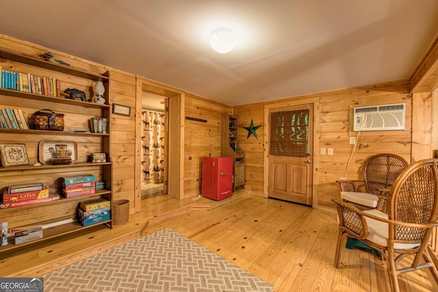 living area with light hardwood / wood-style flooring, wooden walls, and a wall mounted AC