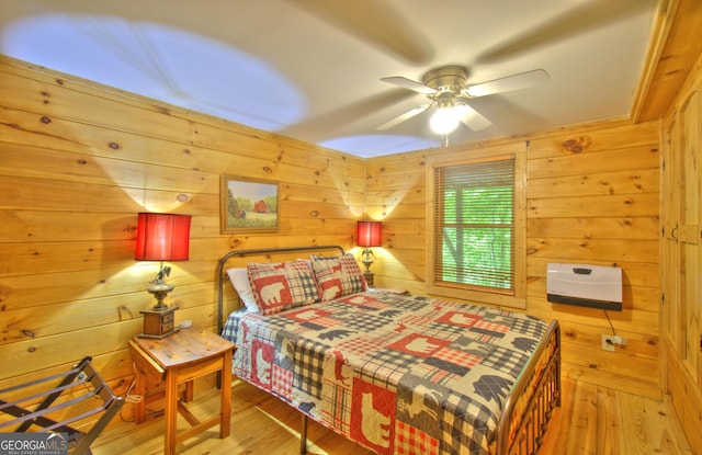 bedroom with ceiling fan, wood walls, and light hardwood / wood-style flooring