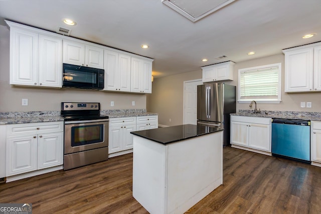 2911 Glenwood Ave SE, Atlanta, GA 30317 - kitchen with white cabinets, a kitchen island, appliances with stainless steel finishes, dark hardwood / wood-style flooring, and light stone countertops