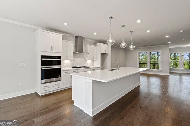 kitchen with white cabinetry, dark wood-type flooring, wall chimney exhaust hood, stainless steel appliances, and a large island