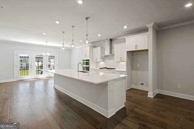 kitchen featuring a large island with sink, white cabinetry, dark hardwood / wood-style flooring, pendant lighting, and wall chimney range hood