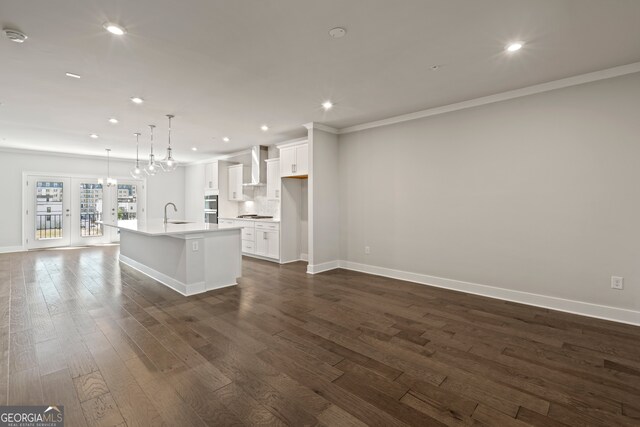 kitchen featuring decorative light fixtures, a kitchen island with sink, wall chimney range hood, white cabinetry, and dark hardwood / wood-style floors